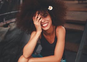Cheerful woman wearing ripped jeans and curly hair with flower, enjoying a sunny day outdoors.